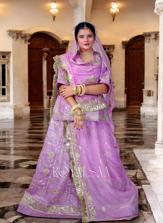 Woman in a purple traditional outfit with gold accents standing in an elegant interior setting.