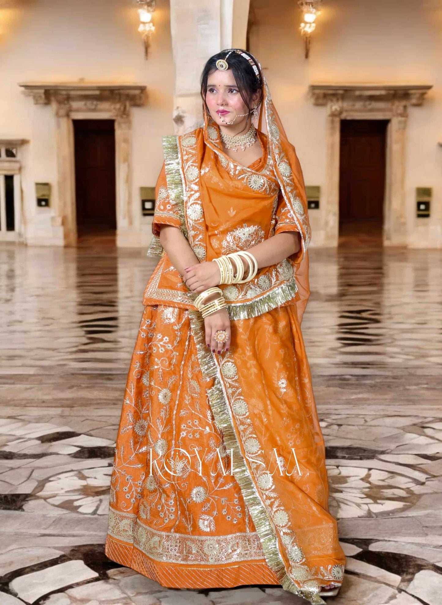 Woman in an orange traditional outfit with gold accents in a formal building setting