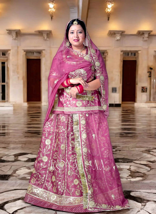 Woman in a traditional pink embroidered outfit standing in an elegant indoor setting.